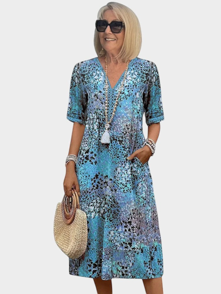 Victoria Boutique midi dress in blue abstract print with V-neckline, short sleeves, and side pockets on a woman.