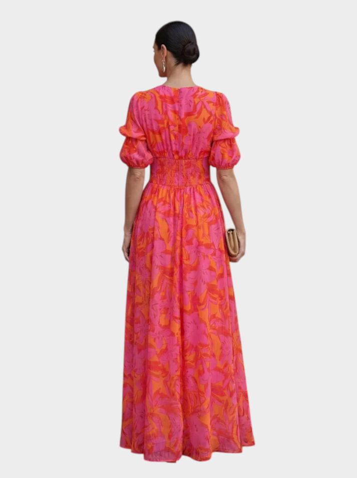Back view of a woman wearing a Victoria Boutique floral maxi dress in vibrant pink and coral with puff sleeves.