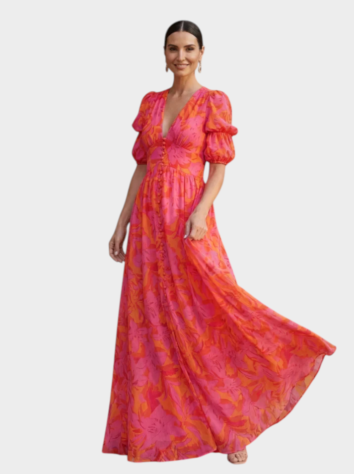 Victoria Boutique floral maxi dress in pink and coral with puff sleeves and a button-down front on a smiling model.